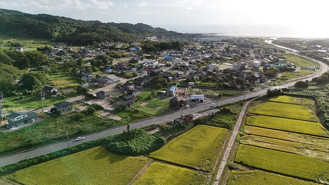 海と山に囲まれた道下地区の空撮。田畑の中に住宅が立ち並ぶ集落の全景